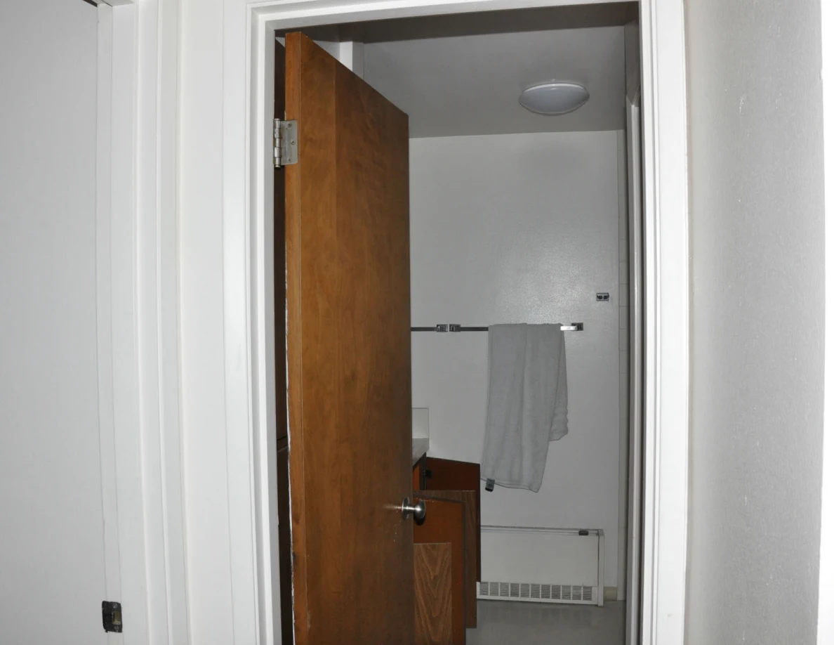 Bathroom doorway with an open wooden door, hanging towel and wall heater.