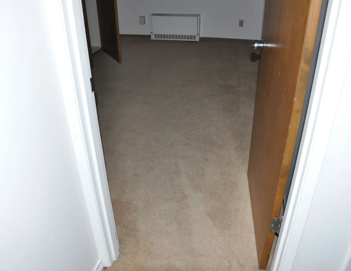 Beige carpet through an open doorway toward a wall heater.