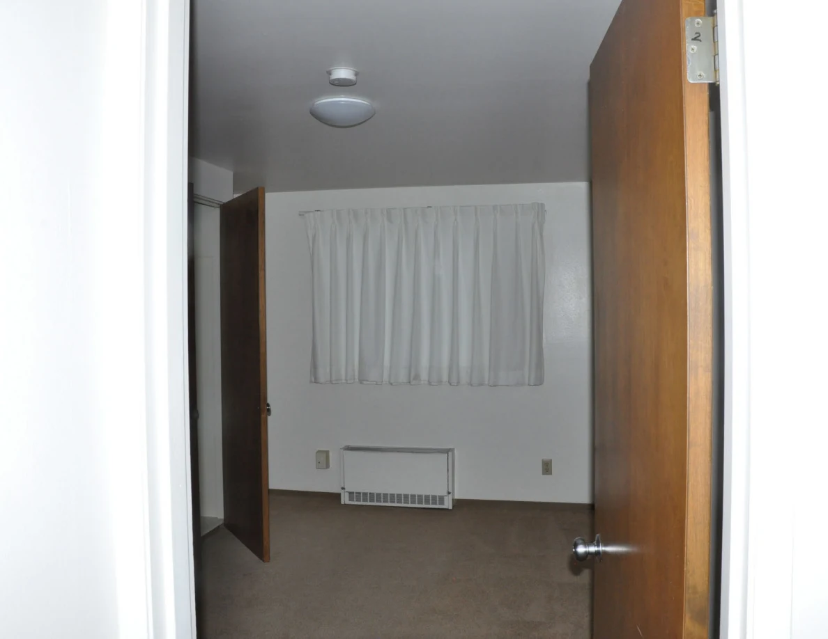 Empty room viewed through a doorway, with curtains, wall heater and ceiling light.