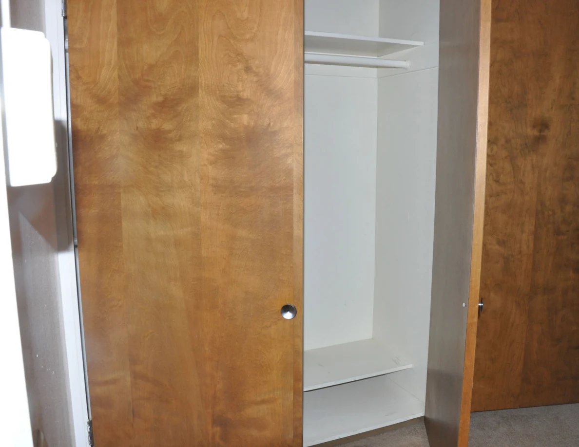 Open wooden closet doors revealing an empty hanging rail and white shelves.