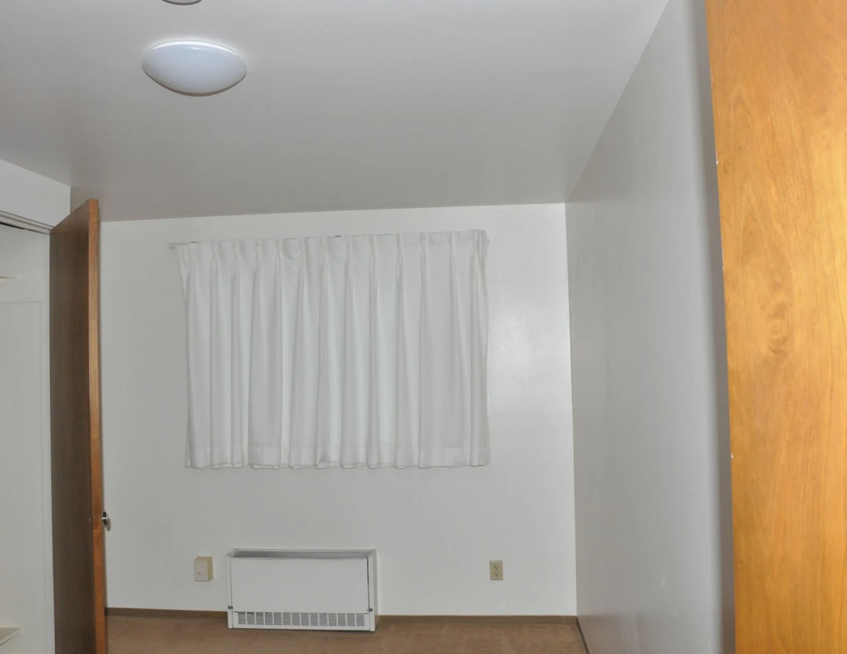 Empty room with white curtains, wall heater and ceiling light.