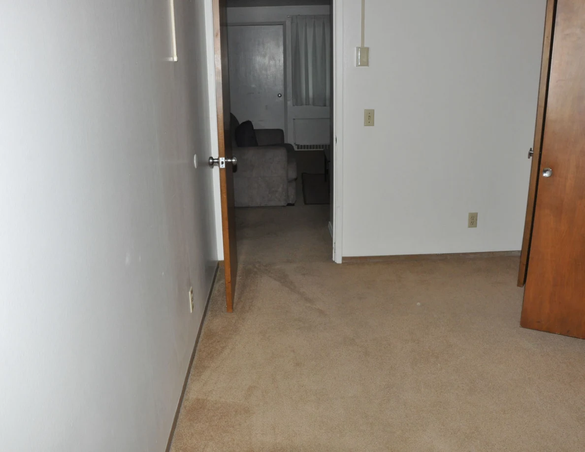 Empty carpeted room looking through a doorway toward the living room.