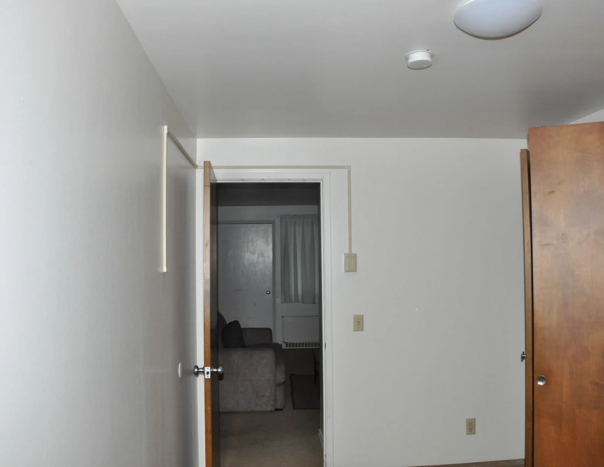 Plain room walls, ceiling light and smoke alarm above an open doorway.