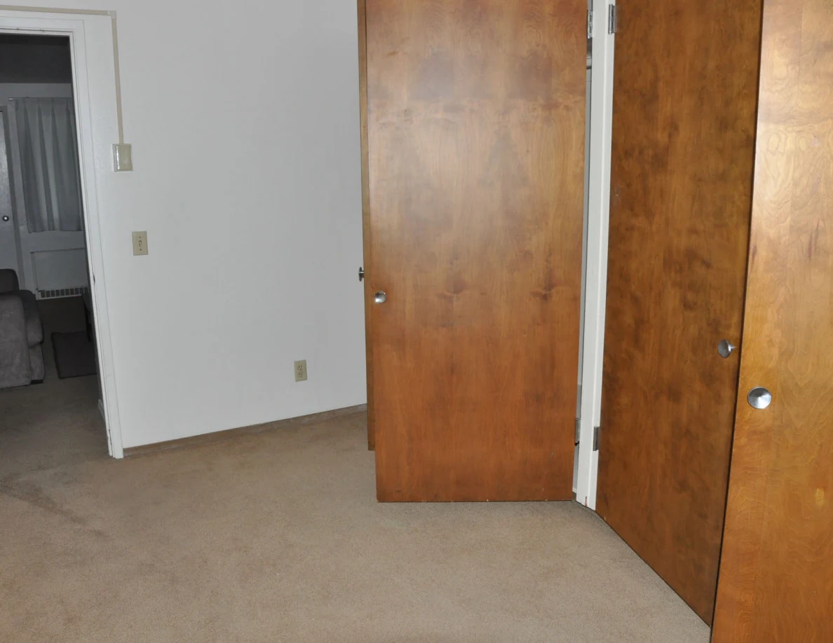 Open wooden closet doors and beige carpet beside a doorway.