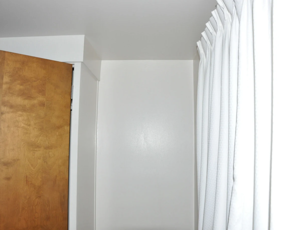 Room corner with an open wooden closet door beside white curtains.