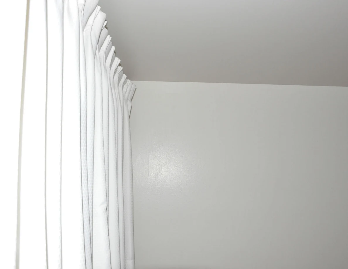 Upper corner of a plain room beside white curtains.
