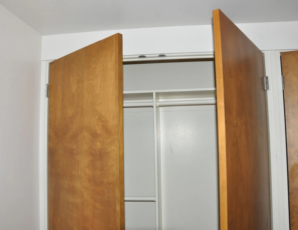 Open wooden closet doors revealing empty hanging rails and an upper shelf.