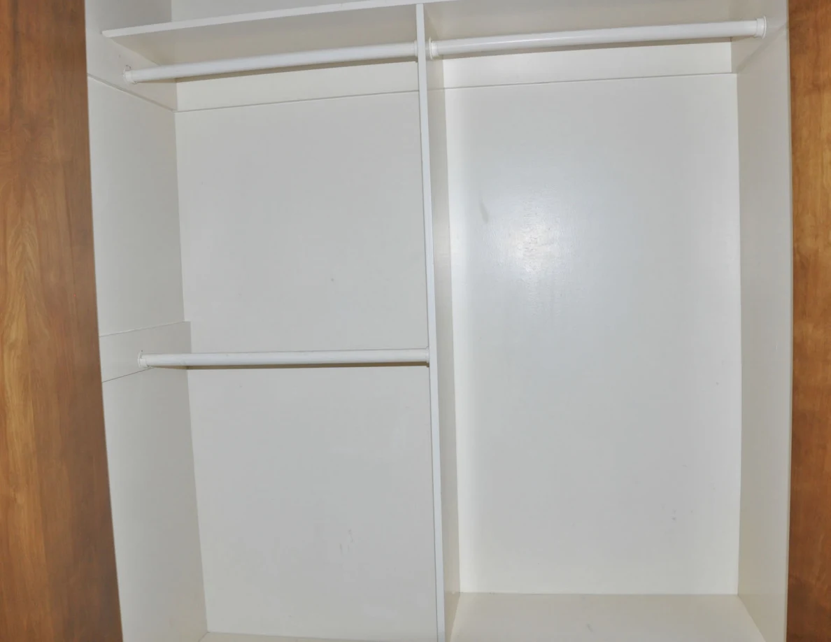 Empty white closet interior with hanging rails and a central divider.
