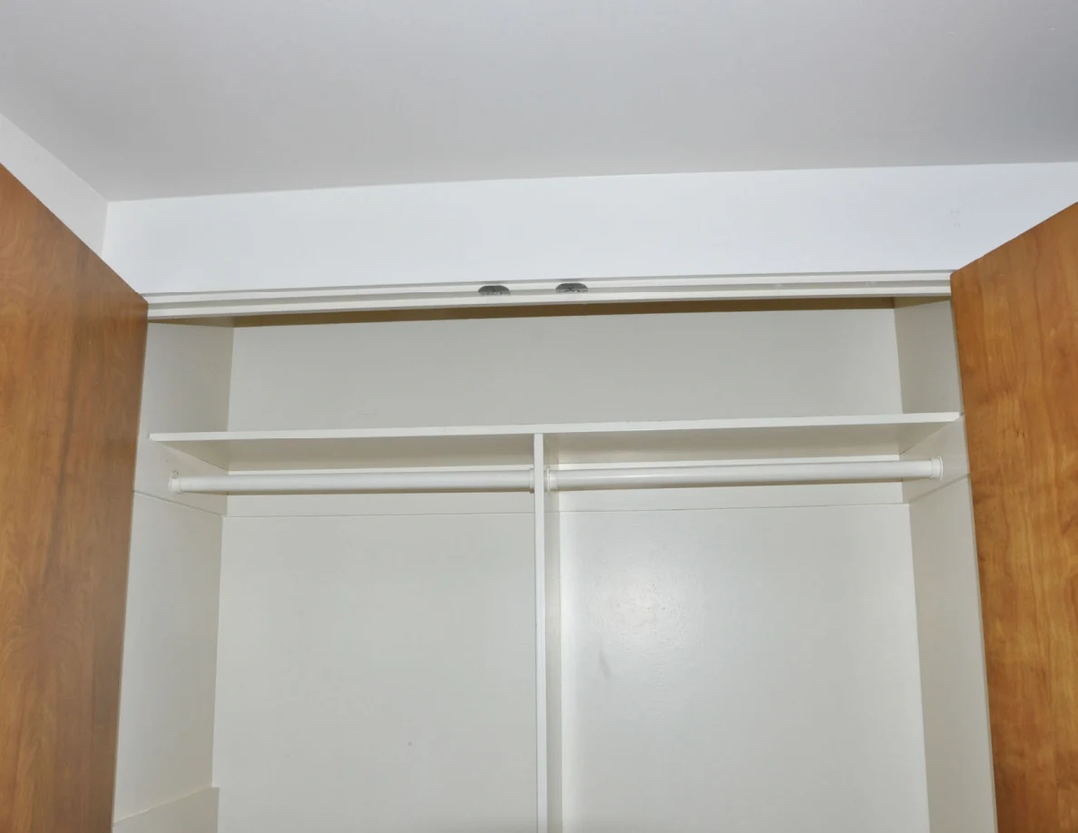 Upper closet shelf and two hanging rails framed by open wooden doors.