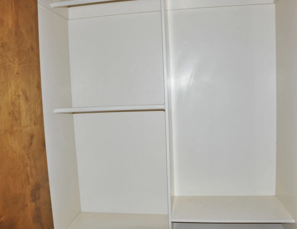 Empty closet with hanging rails, central divider and lower shelf.