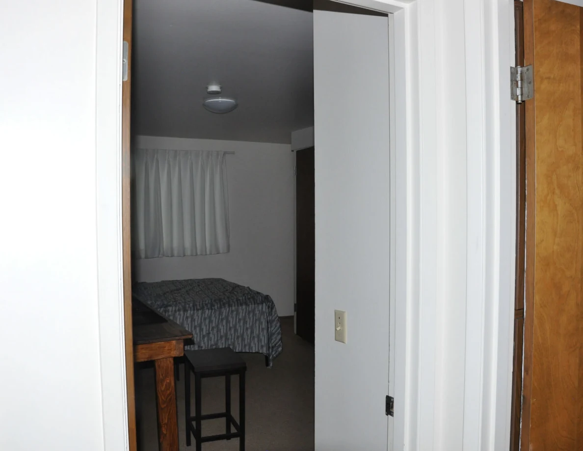 Bedroom entrance showing a bed below curtains and a ceiling light.