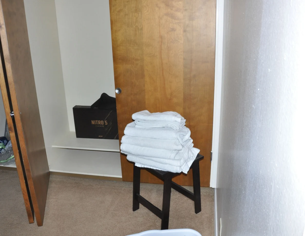 Folded white towels stacked on a black stool beside an open closet and Nitro 5 box.