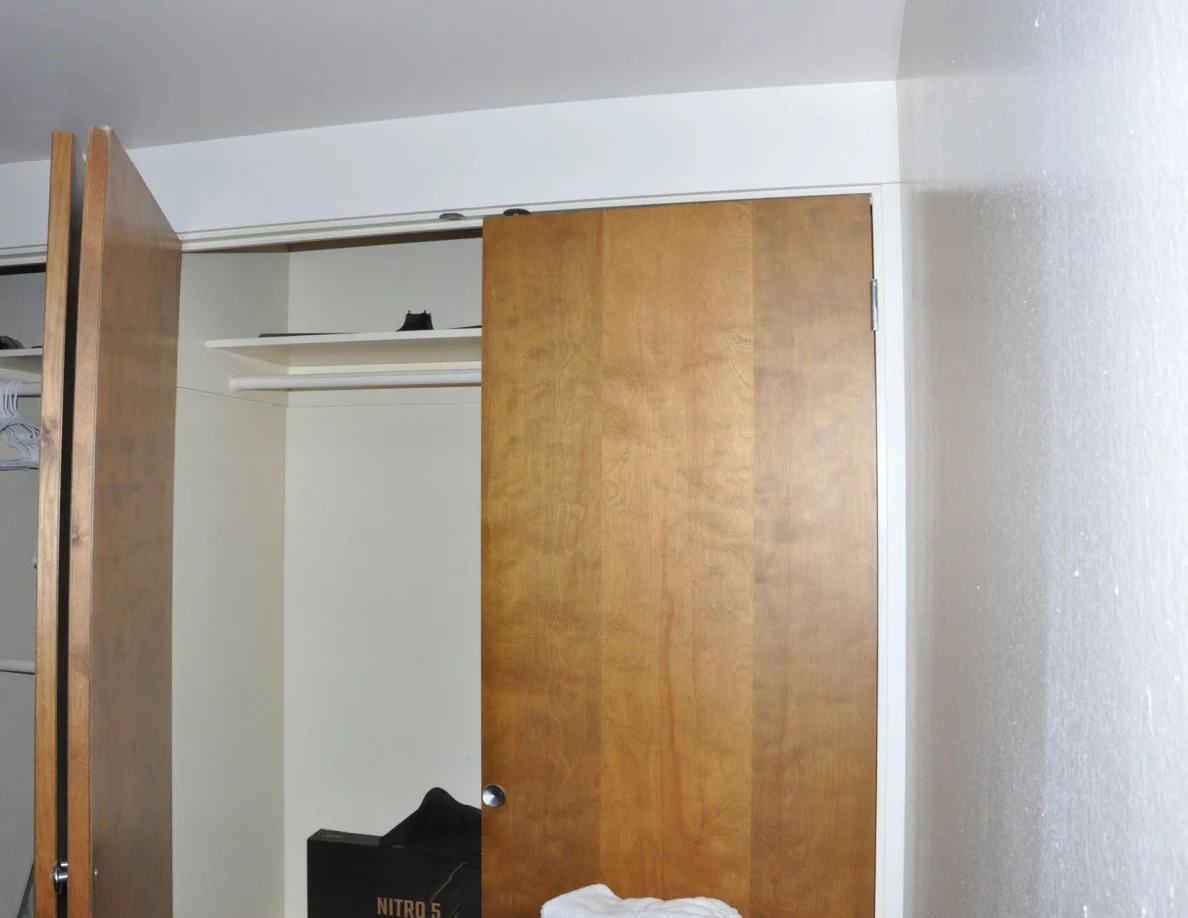 Upper open closet with a wooden sliding door and mostly empty white shelving.