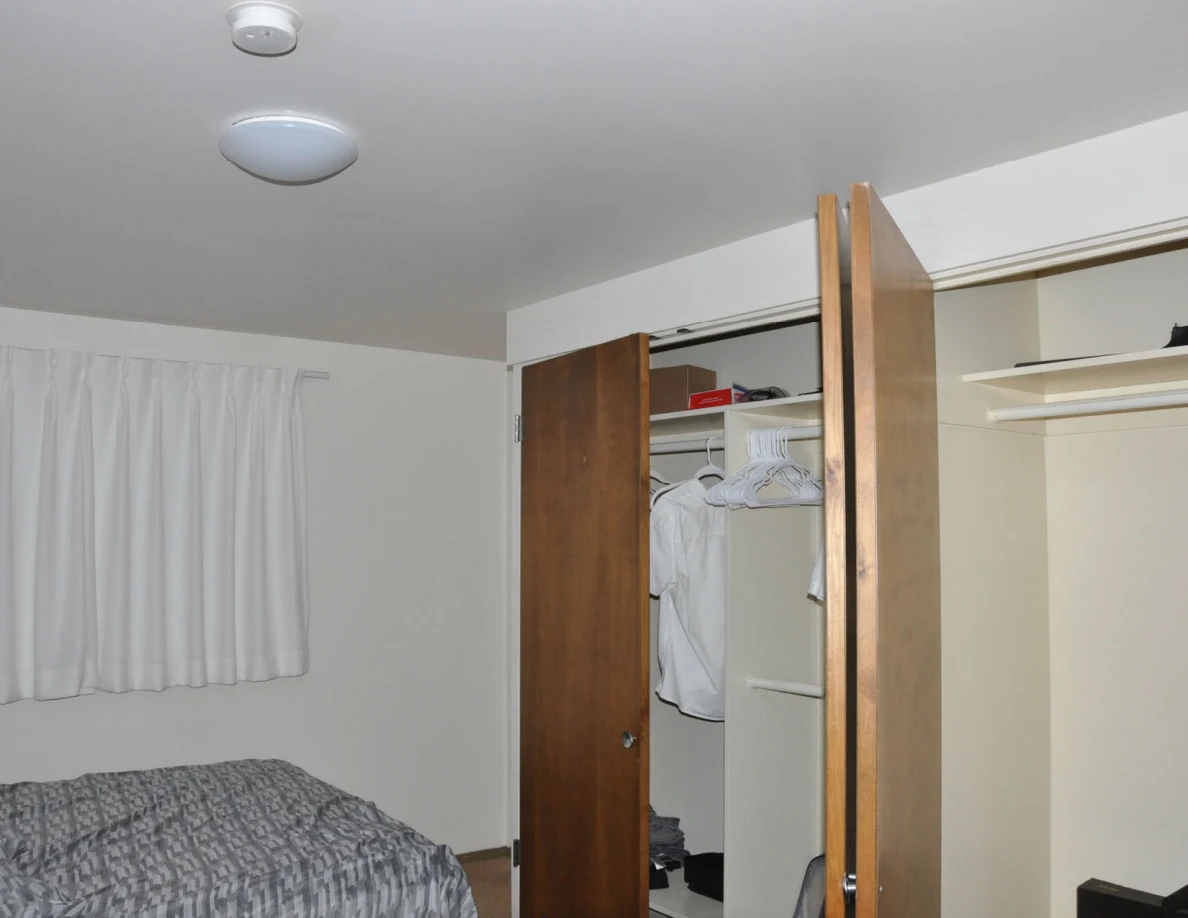 Bedroom with bed, open closets, hanging shirts, curtains and a ceiling light.