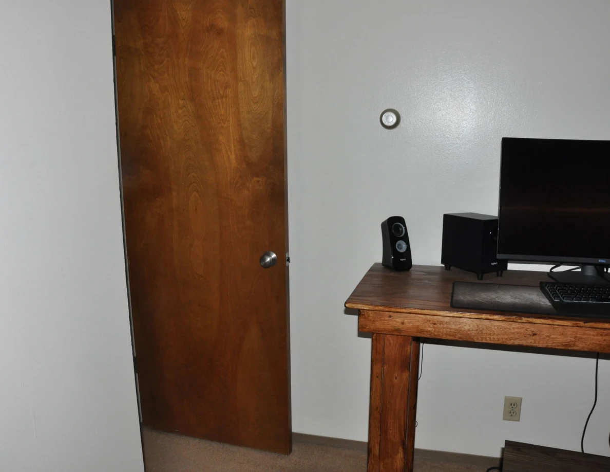 Wooden bedroom door and computer desk with monitor and speaker.
