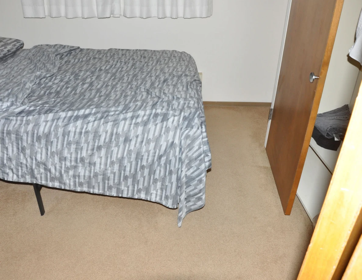 Foot of a bed with a gray patterned cover beside an open closet.