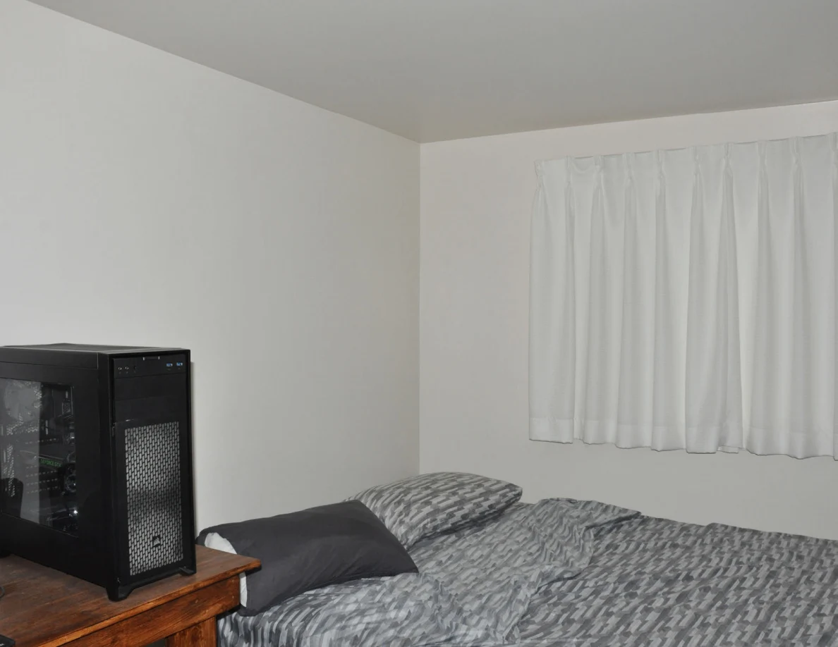 Bedroom corner with a computer tower, bed and curtains.