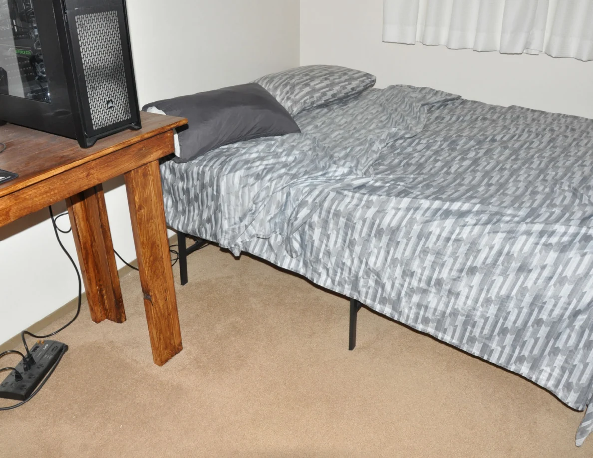 Bed with gray patterned cover and two pillows beside a wooden computer desk.