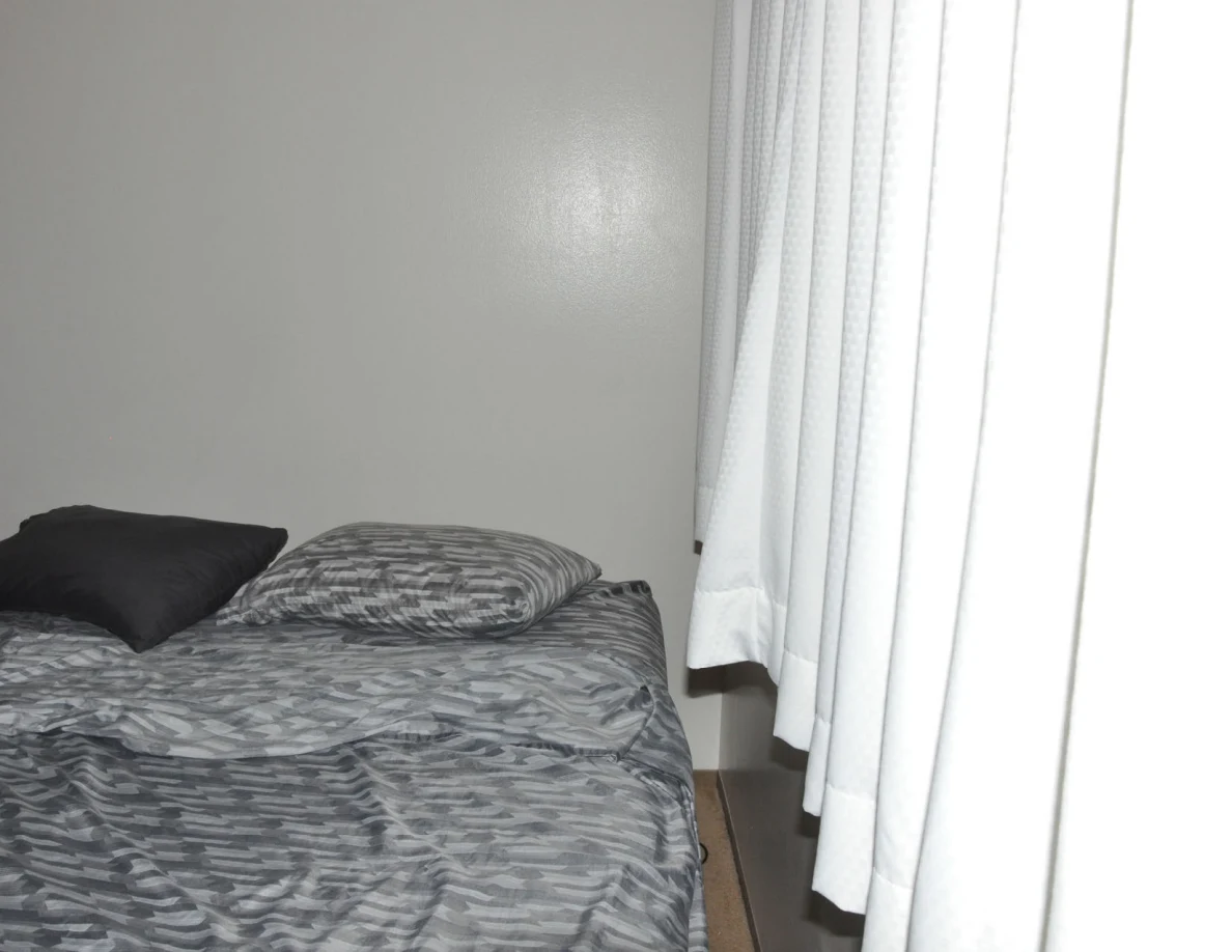 Head of a bed with dark and patterned pillows beside white curtains.