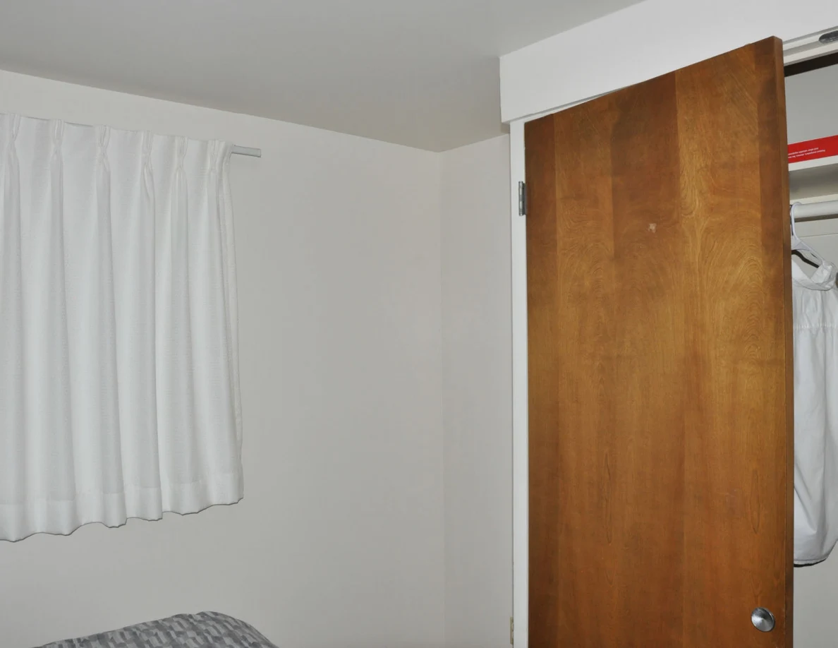 Bedroom corner with white curtains and wooden closet doors.