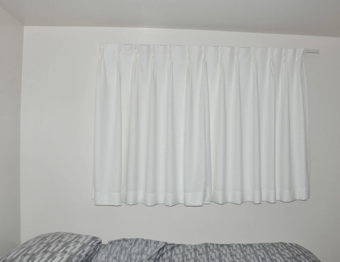 Closed white curtains above the head of a bed.