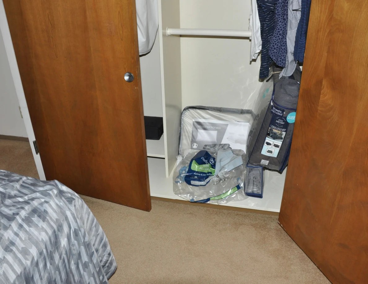 Open closet bottom shelf with packaged bedding beneath hanging shirts.