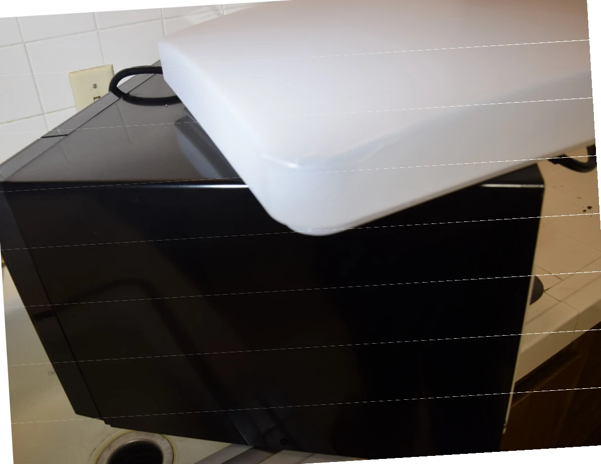 White rectangular light cover resting on a black countertop appliance; horizontal bands cross the photo.