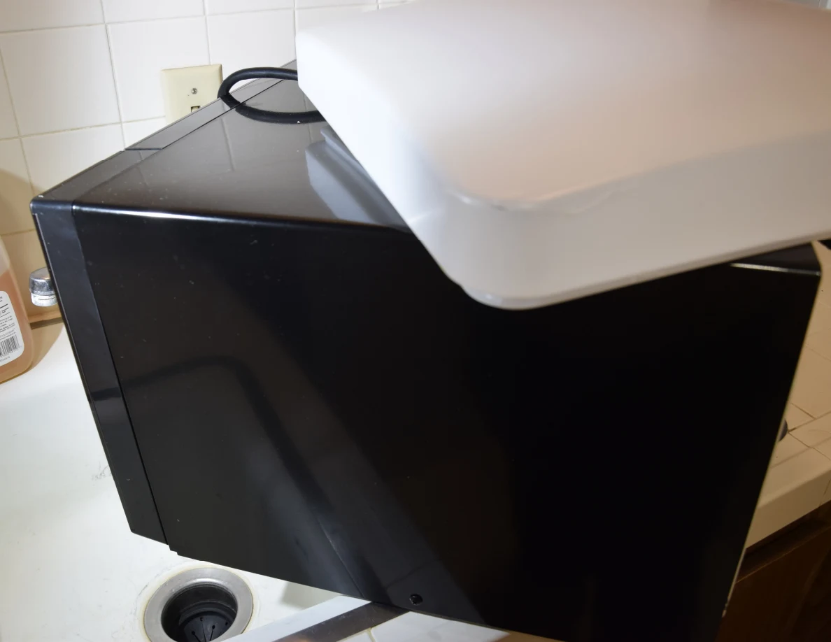 White light cover on top of a black countertop appliance beside a sink.