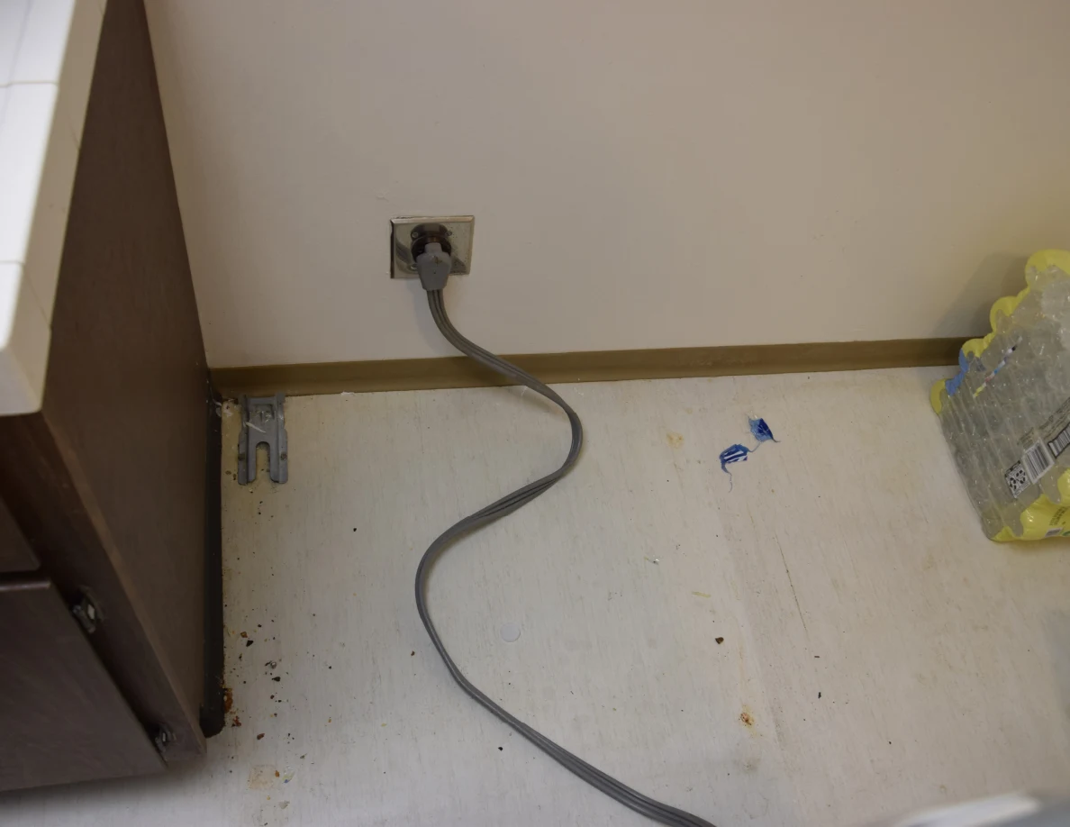 Floor behind a moved kitchen range, with power cord, scattered debris and packs of drinks.