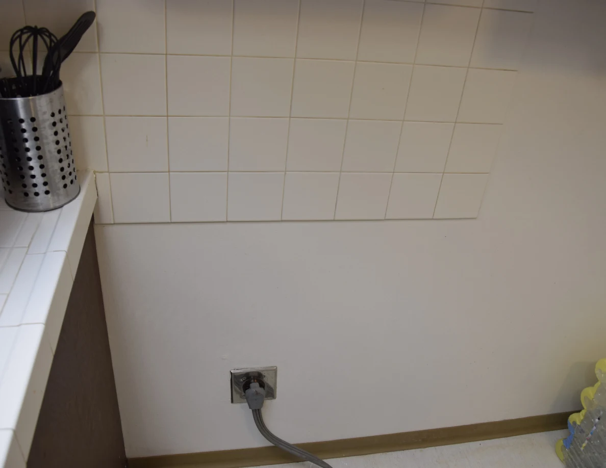 Wall and tiled backsplash behind a moved range, with electrical outlet and cord.