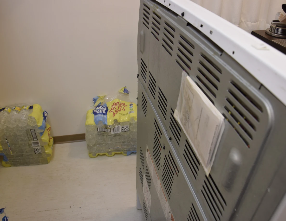 Vented metal back of a moved kitchen range beside packs of drinks.