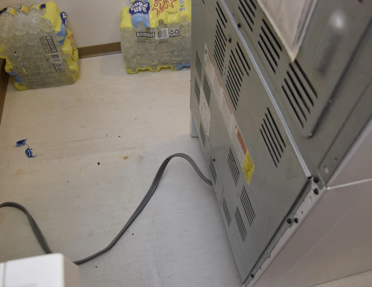 Lower back of a kitchen range with power cable crossing pale flooring.