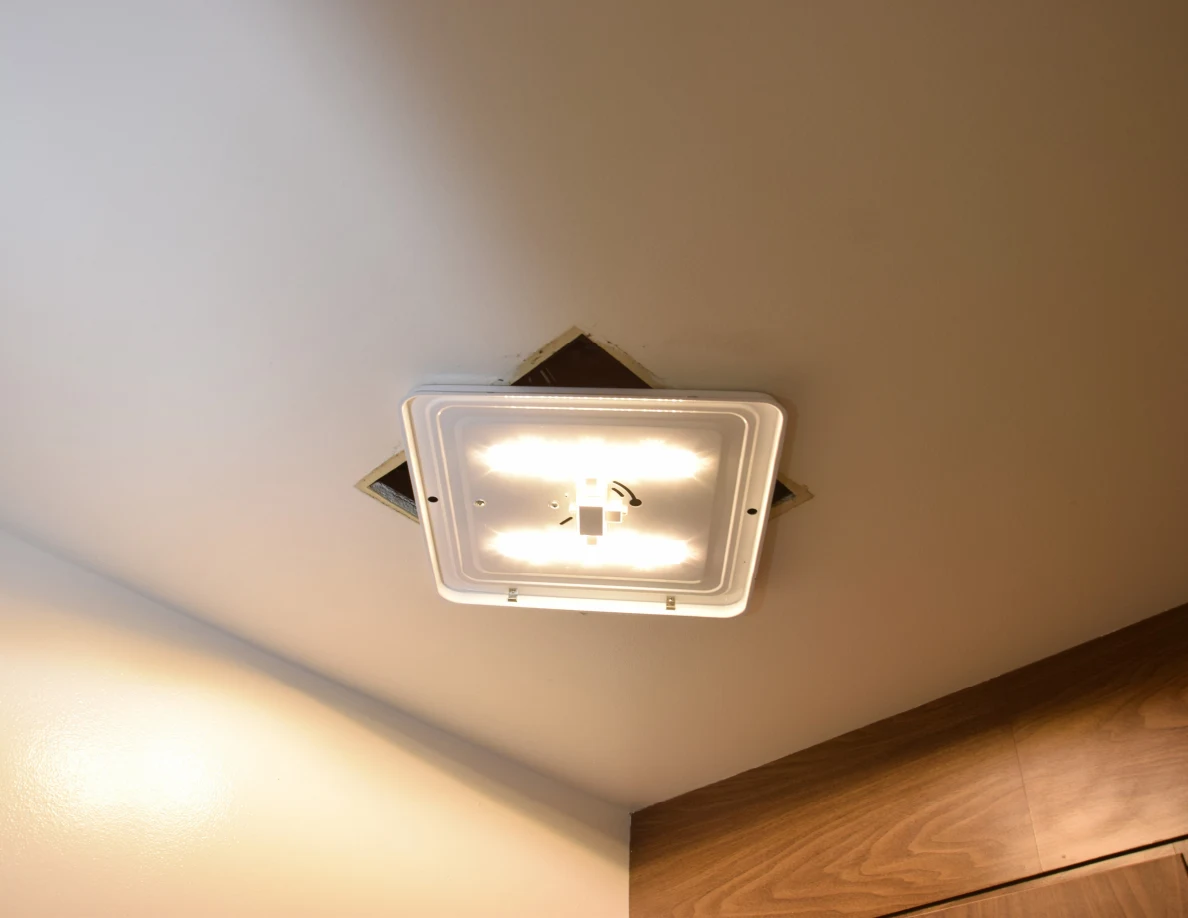Illuminated ceiling light with its cover removed, exposing the surrounding ceiling opening.