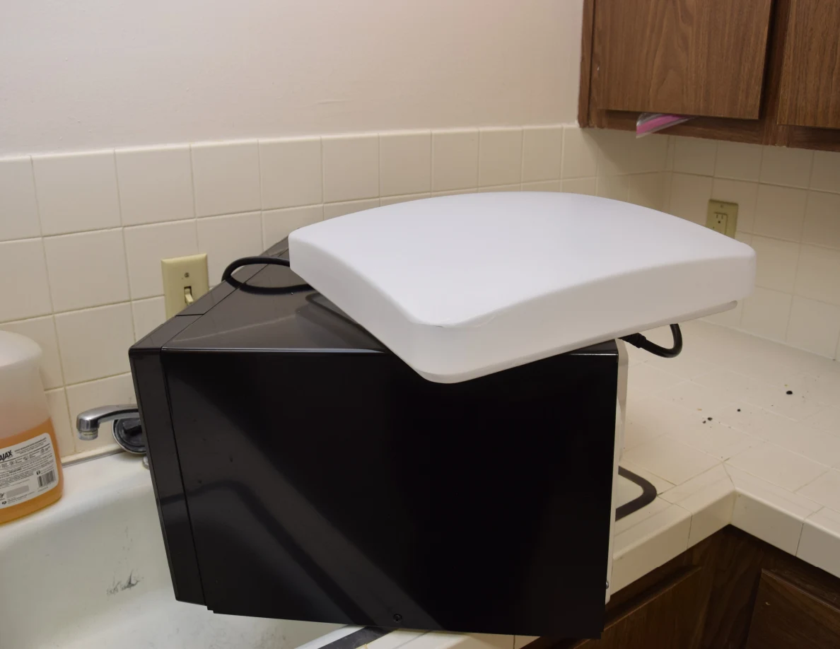 White light cover resting on a black appliance beside a kitchen sink and tiled counter.