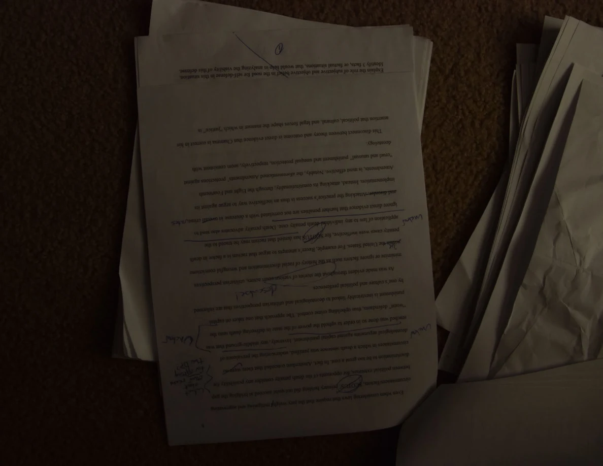 Dim upside-down printed essay page with handwritten notes on a stack of papers.