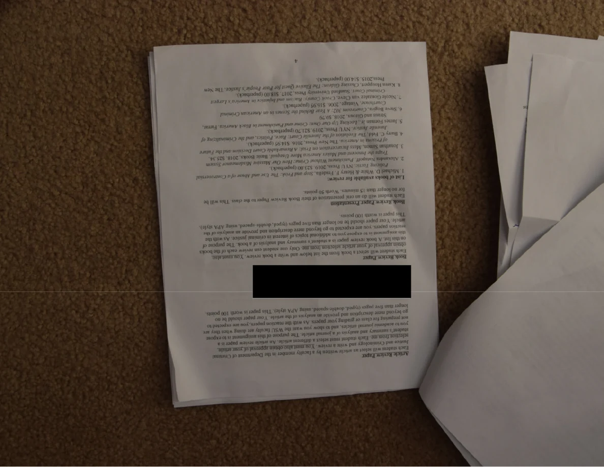 Upside-down course handout with a black redaction and reading-list text.
