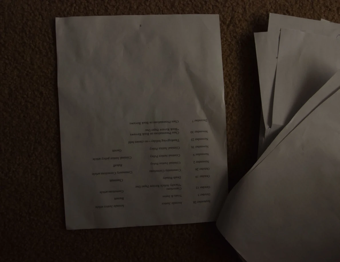 Dim creased schedule page photographed upside down on carpet.
