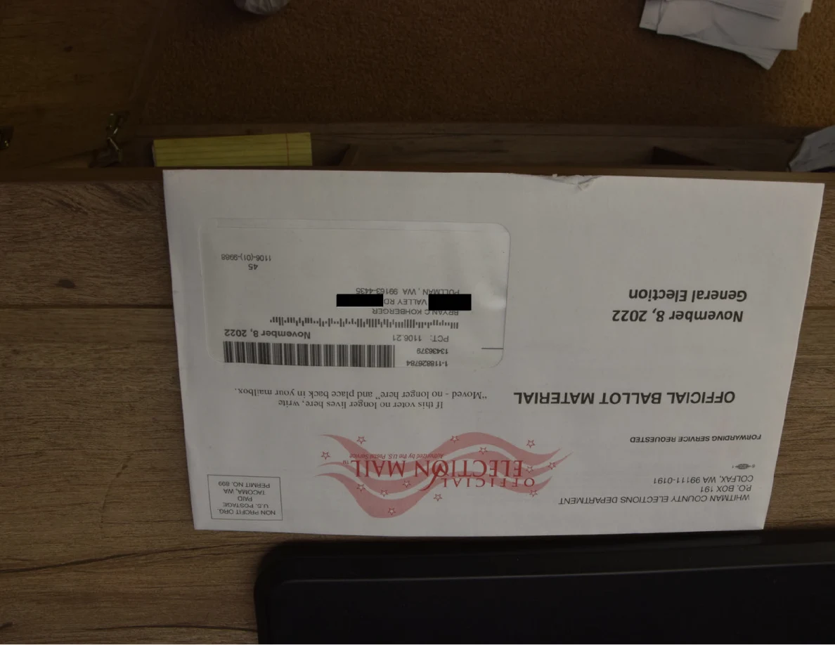 Official ballot-material envelope on a wooden surface with black redactions over address details.