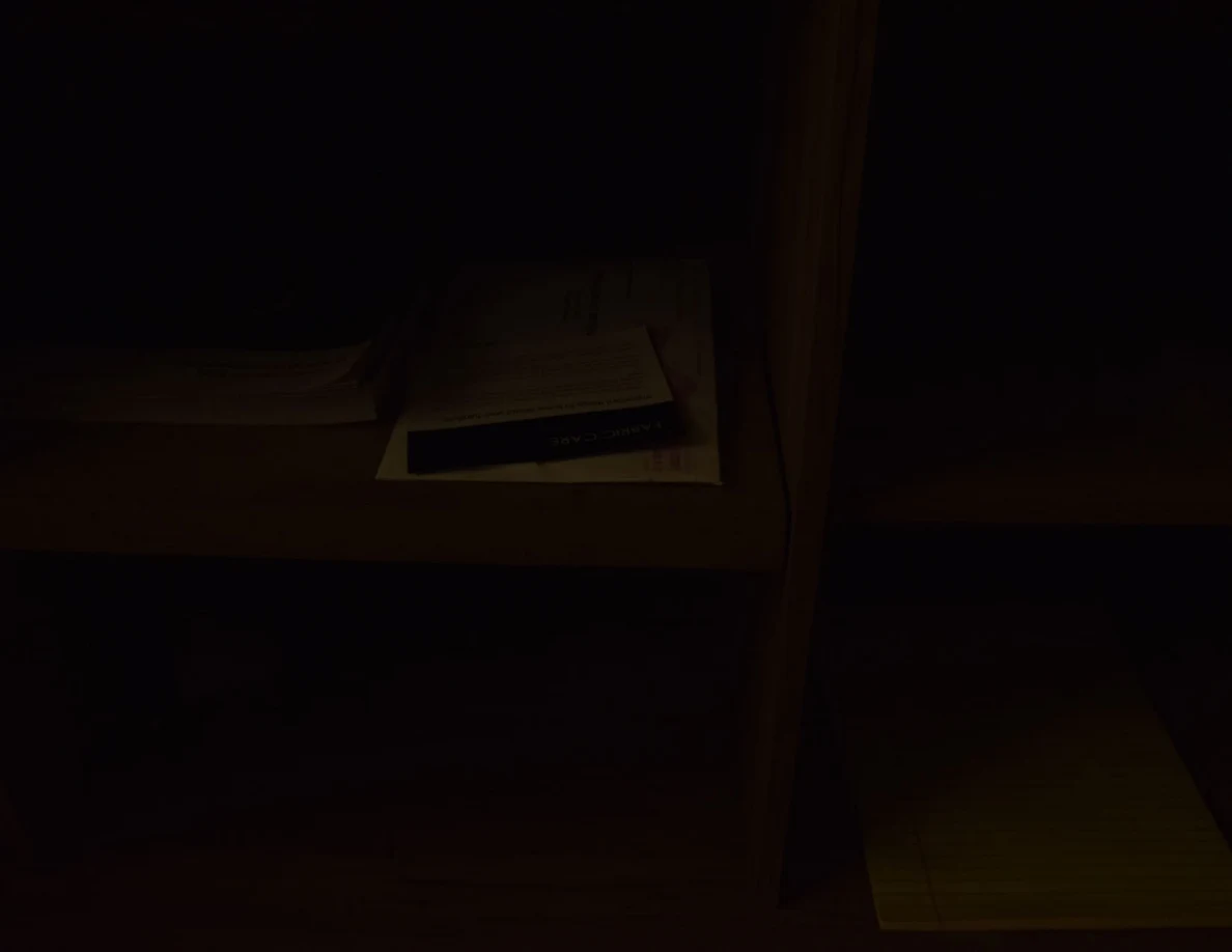 Very dark photograph of wooden cabinet shelves with papers and a yellow notepad.