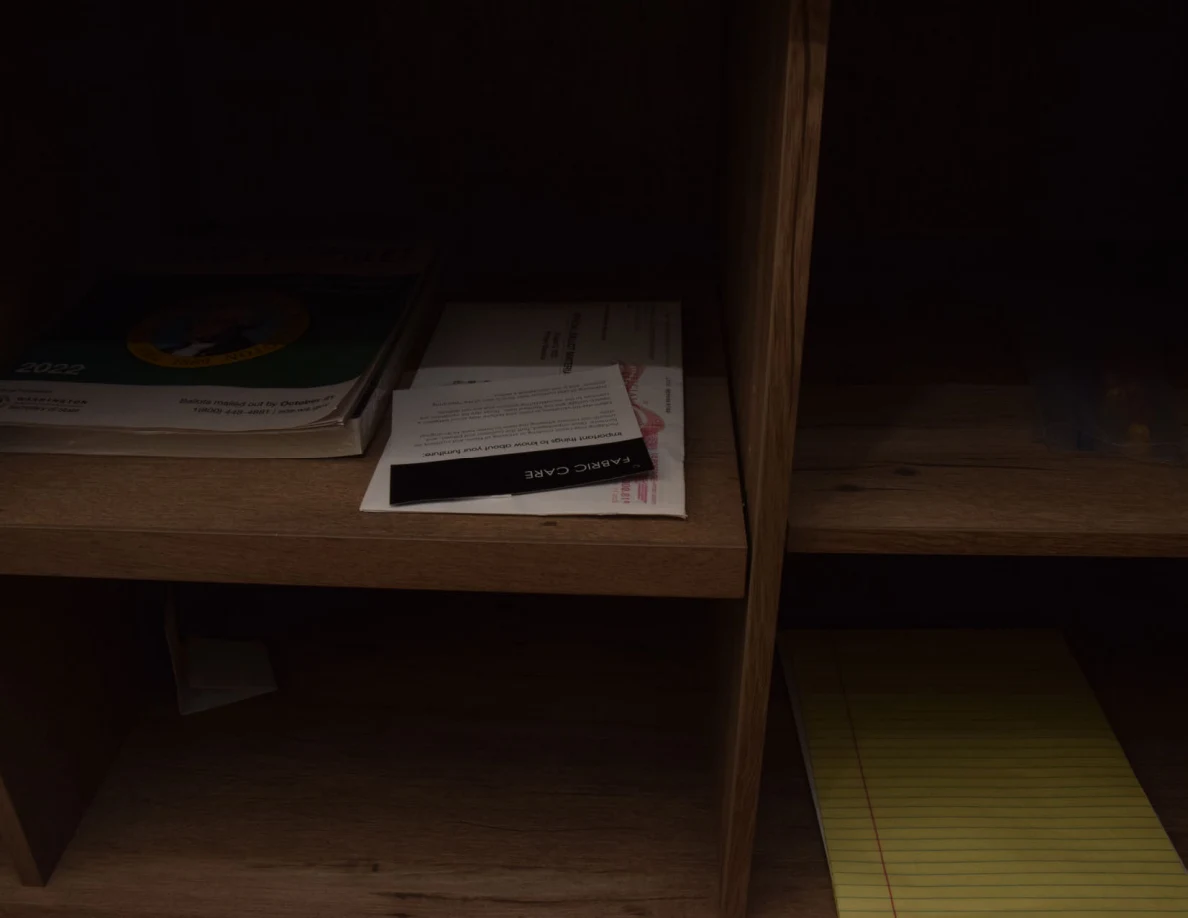 Dim open cabinet shelves with books, mail and a yellow writing pad.