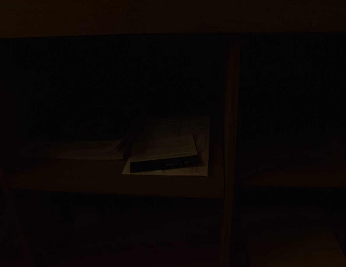Very dark close view of cabinet shelving with a small stack of papers.