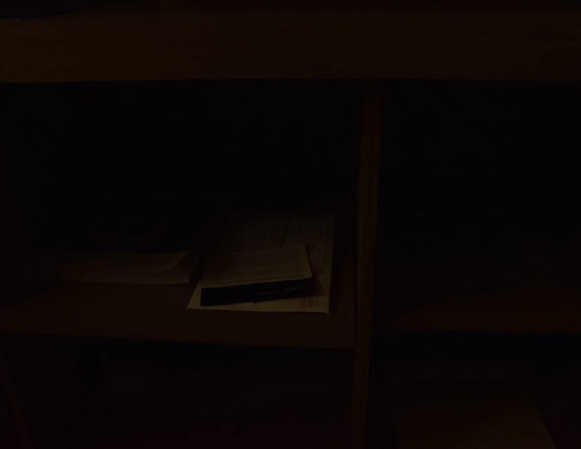 Very dark view of cabinet shelves containing paper stacks and a yellow notepad.