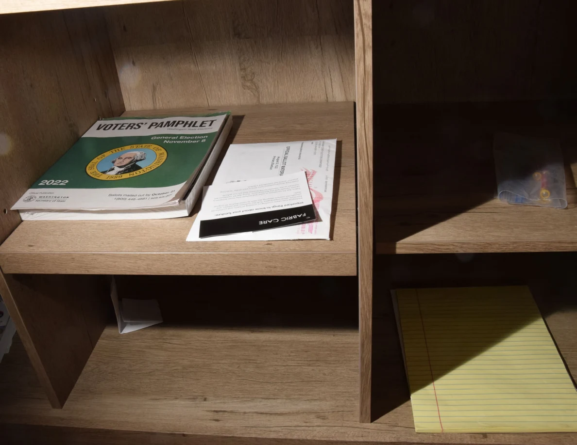 Cabinet shelves containing a voters pamphlet, mail and a yellow lined notepad.