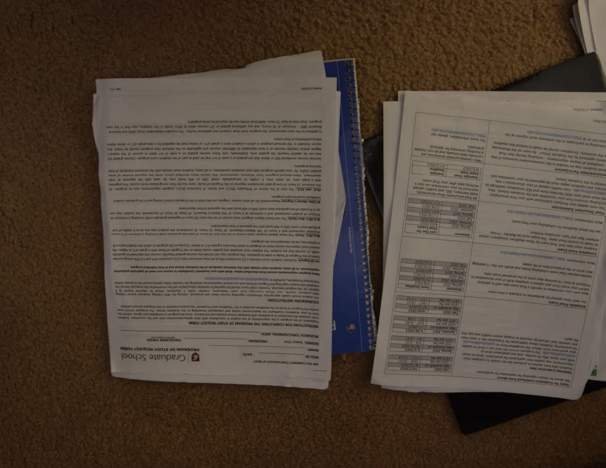 Printed graduate-school form and instructional handouts lying upside down on carpet.