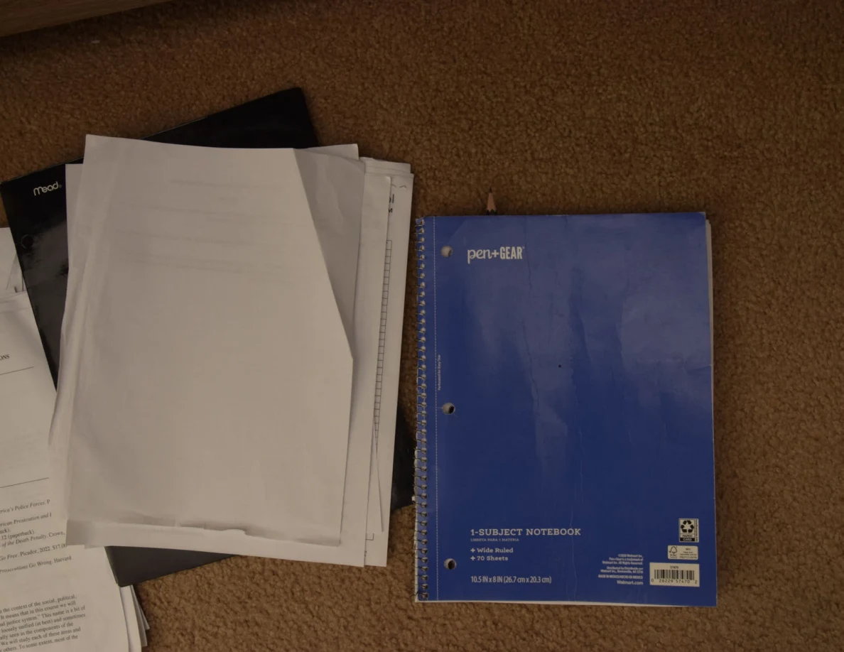 Blue spiral notebook beside a stack of loose white papers.