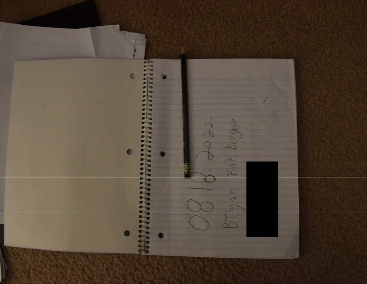 Open lined notebook with a pencil, handwritten heading and black redaction.
