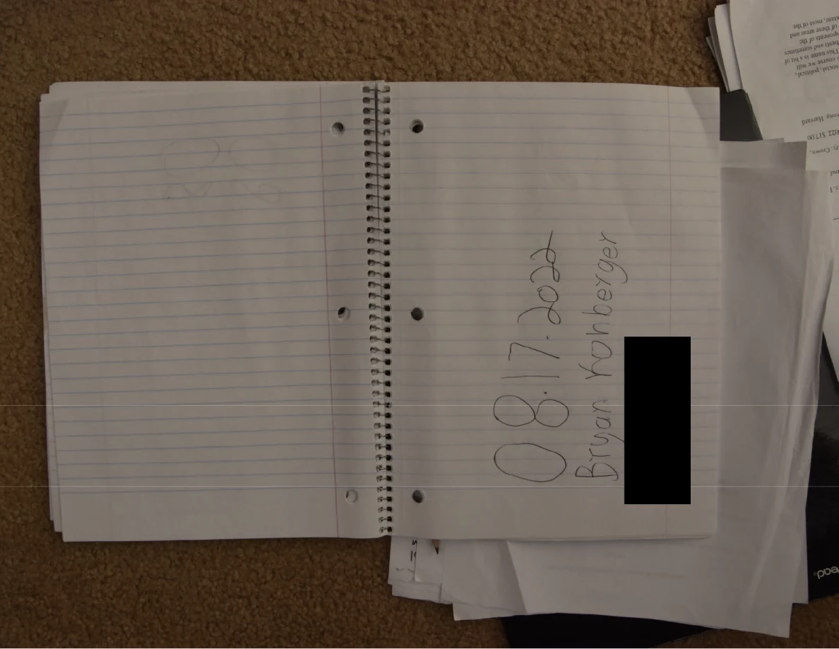 Open lined notebook with a handwritten heading and black rectangular redaction.