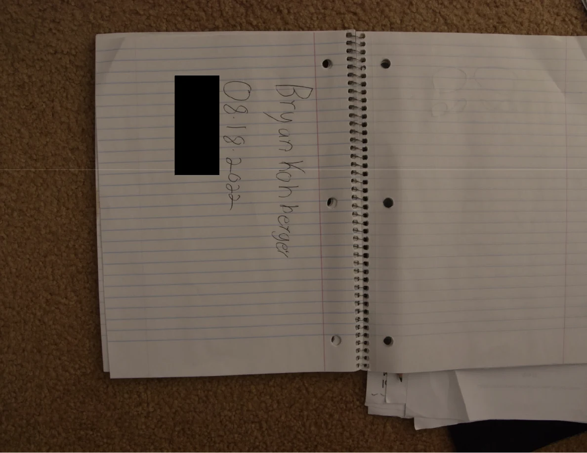 Open lined notebook with handwritten heading and a black redaction.