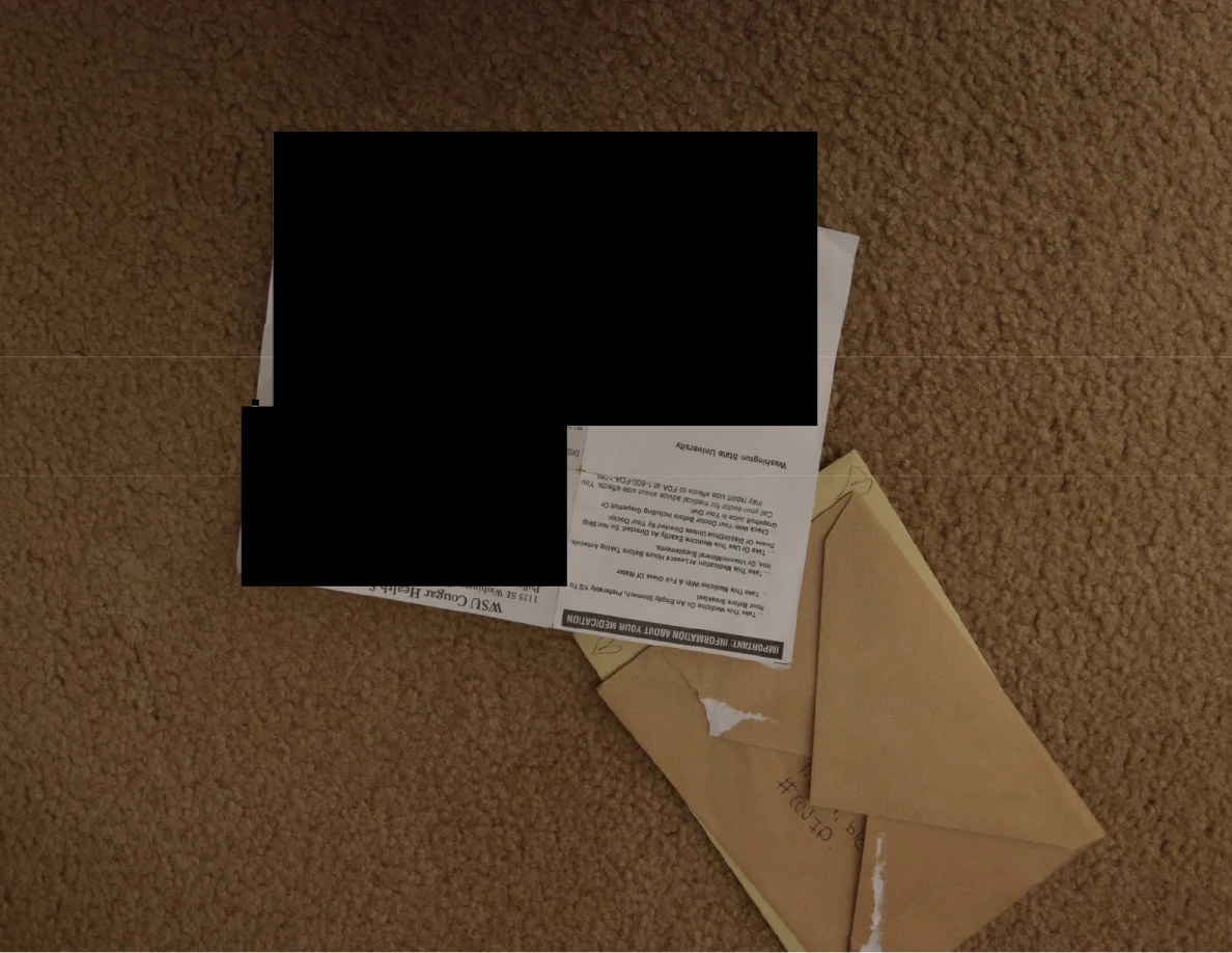 Mail and envelopes on carpet with a large black redaction covering most of one sheet.