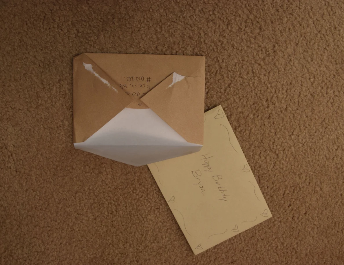 Open brown envelope beside a yellow birthday card on carpet.